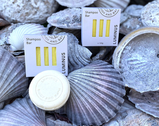 Quench Shampoo boxes on a natural shell surface with a unwrapped shampoo bar in front