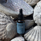 A 30ml amber glass dropper bottle of Luminus South beard oil, nestled among natural gray seashells and driftwood.